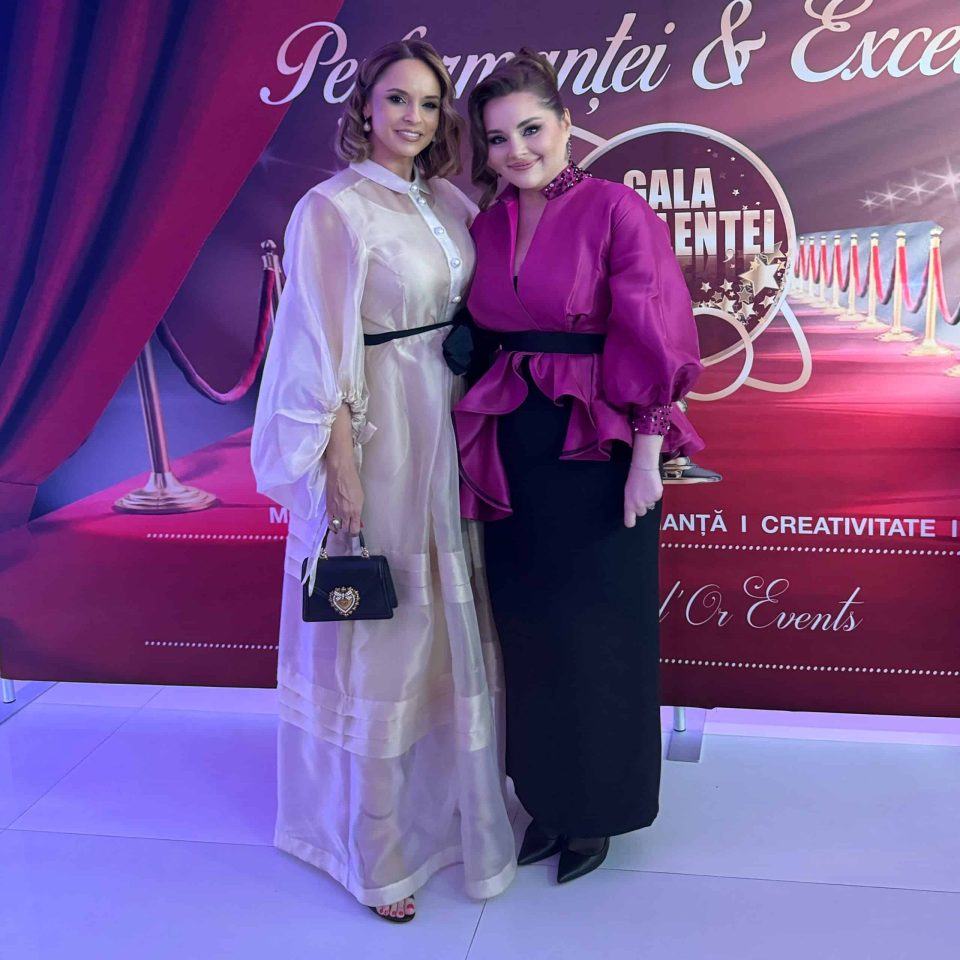 Două persoane care pozează pe o podea albă curată în fața unui fundal roșu și violet, împodobit cu text și elemente decorative, surprind esența Gala Excelenței și a Performanței 2024 din România.